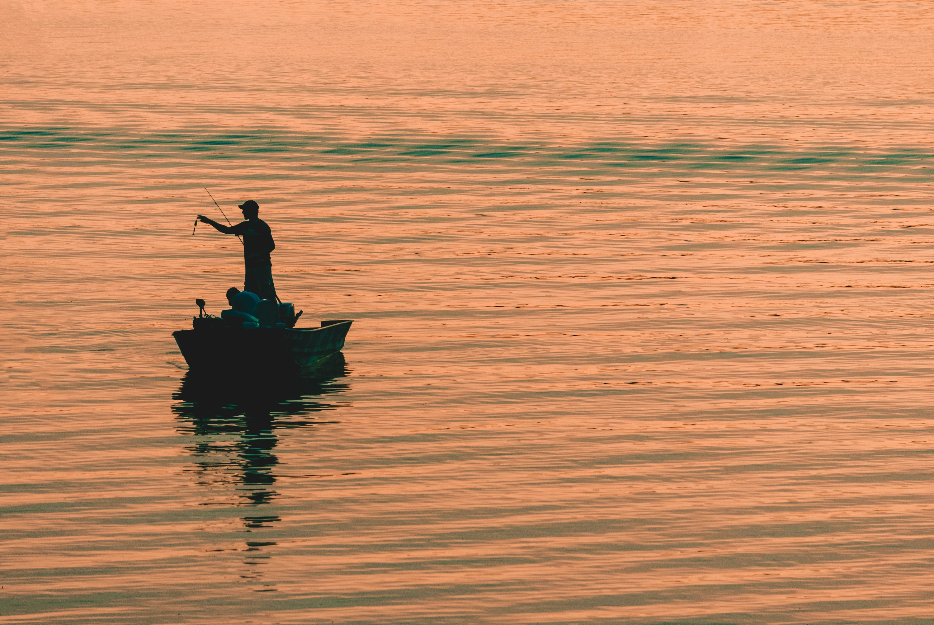 Silhouette of a person fishing on a boat at sunset