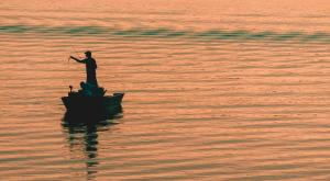 Silhouette of a person fishing on a boat at sunset