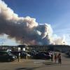 People in a parking lot with large plume of wildfire smoke in background